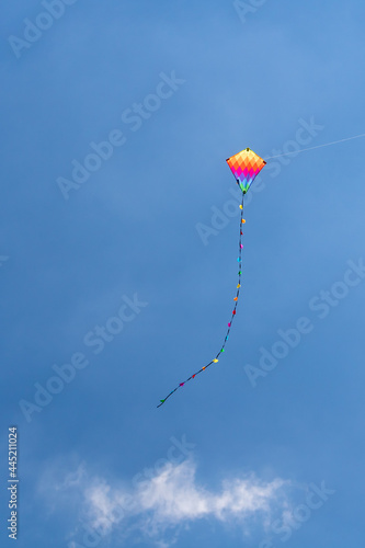 Child's rainbow coloured diamond kite with tail flying high in clear blue summer sky