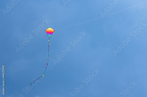 Child's rainbow coloured diamond kite with tail flying high in clear blue summer sky