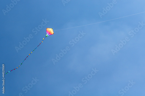 Child's rainbow coloured diamond kite with tail flying high in clear blue summer sky