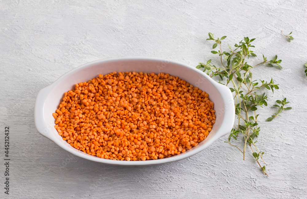 Raw red lentils in a white baking dish with fresh thyme on a light gray background, top view Raw red lentils in a white baking dish with fresh thyme on a light gray background, top view