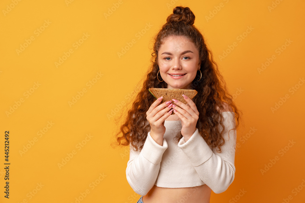 Young woman eating sandwich against yellow background Young woman eating sandwich against yellow background