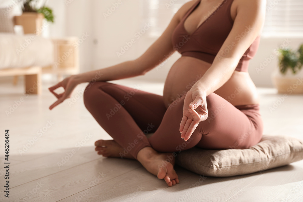 Fototapeta premium Young pregnant woman practicing yoga at home, closeup