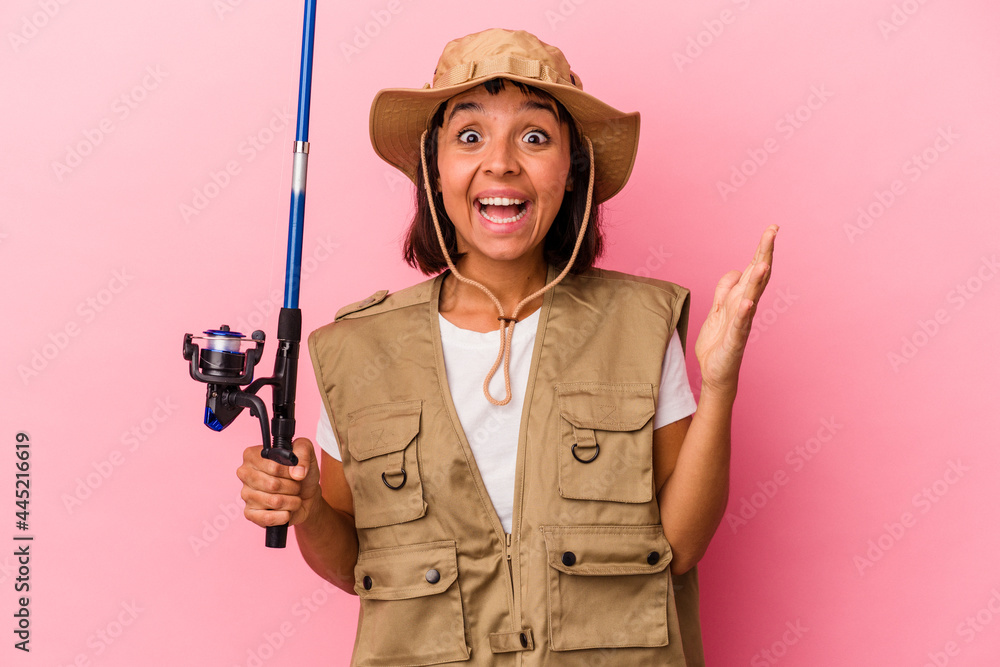 Young mixed race fisherwoman holding a rod isolated on pink background receiving a pleasant surprise, excited and raising hands. Young mixed race fisherwoman holding a rod isolated on pink background receiving a pleasant surprise, excited and raising hands.