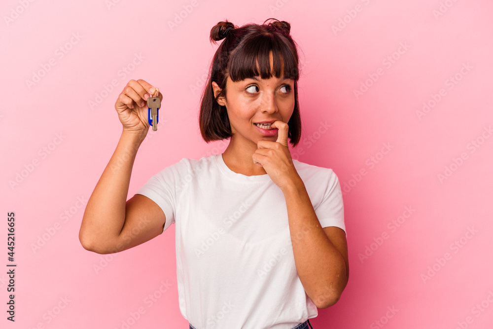 Young mixed race woman holding a keys isolated on pink background relaxed thinking about something looking at a copy space. Young mixed race woman holding a keys isolated on pink background relaxed thinking about something looking at a copy space.