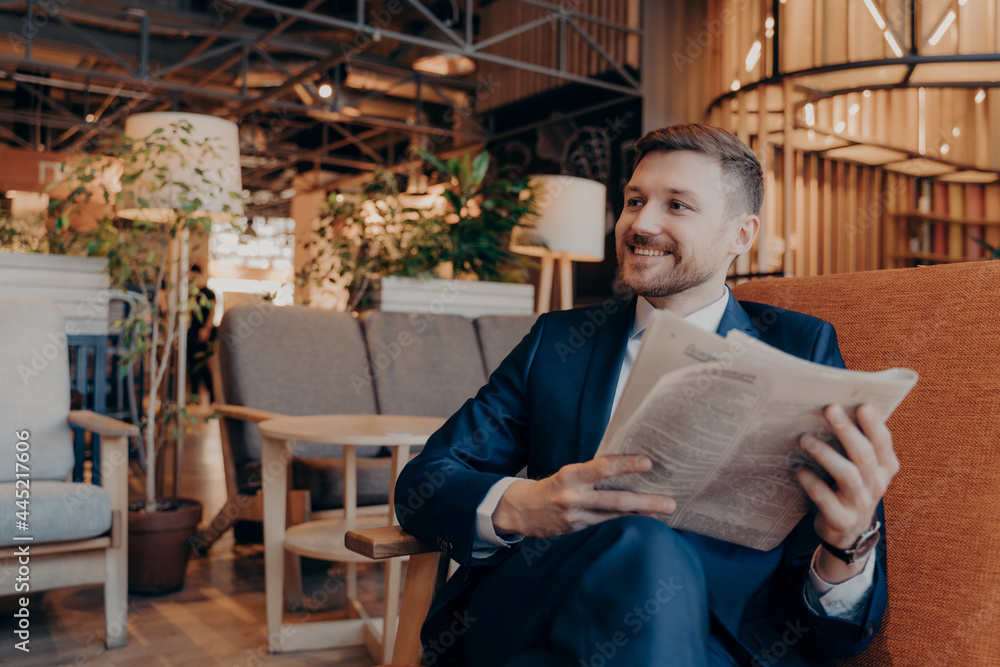 Positive young businessman reading newspaper in cafe