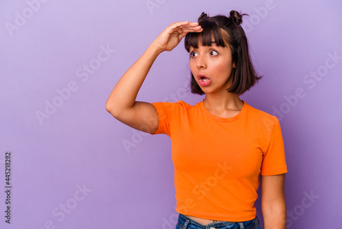 Young mixed race woman isolated on purple background looking far away keeping hand on forehead.