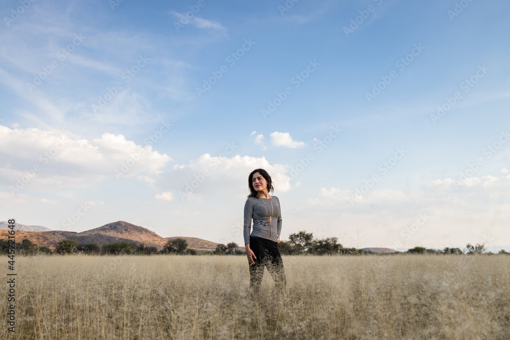 Young adult Mexican woman standing in a dry grassy meadow looking away