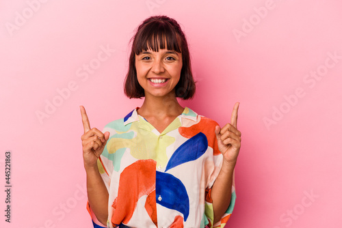 Young mixed race woman isolated on pink background indicates with both fore fingers up showing a blank space.