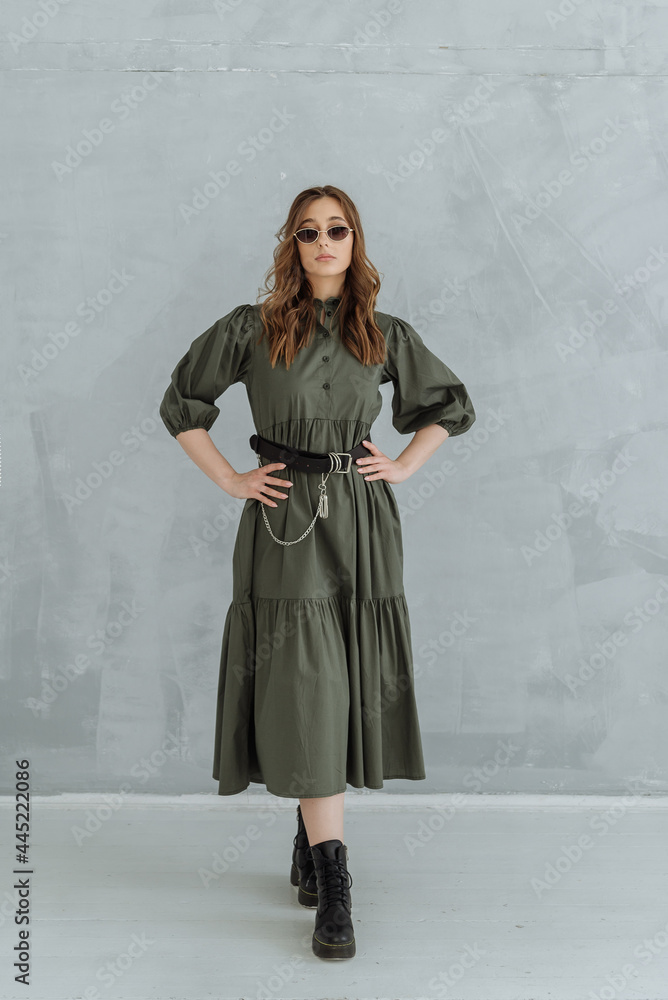 Naklejka premium a woman in a green long dress, sunglasses and rough black shoes on a gray background. trending women's fashion clothing 2021.