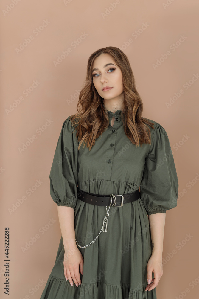 portrait of a beautiful young woman in a green dress with a black waist belt on a brown background. trending women's fashion clothing 2022. a beautiful combination of colors in fashion portrait of a beautiful young woman in a green dress with a black waist belt on a brown background. trending women's fashion clothing 2022. a beautiful combination of colors in fashion