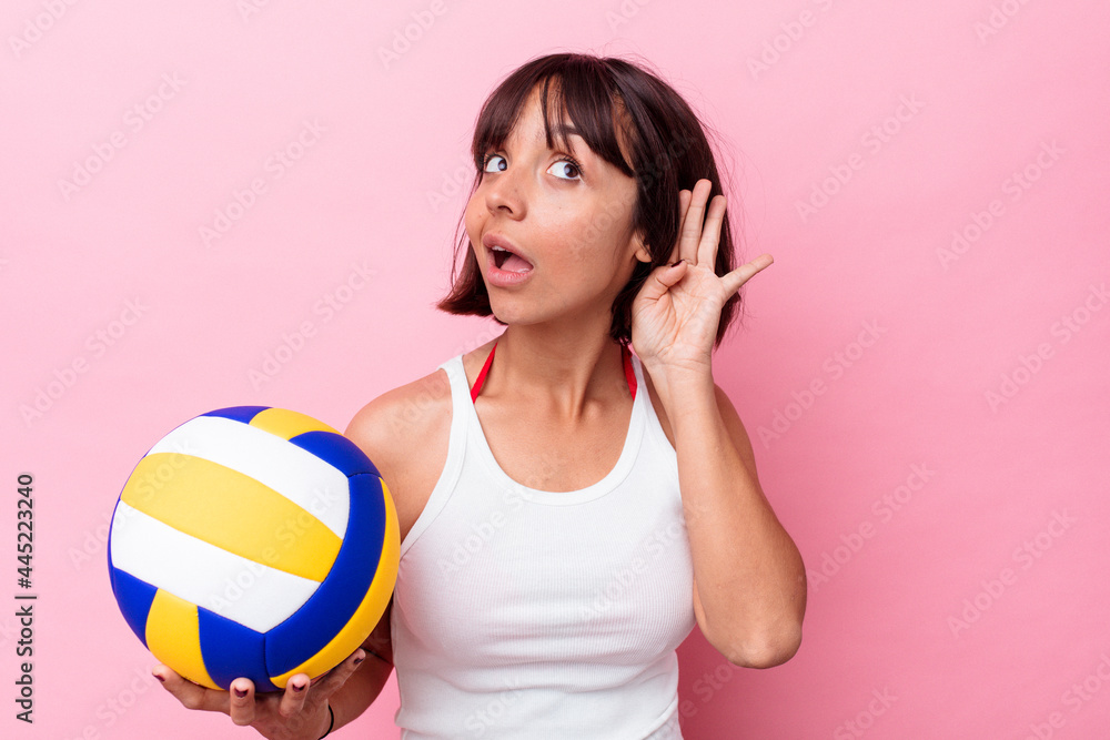 Young mixed race woman playing volleyball isolated on pink background trying to listening a gossip. Young mixed race woman playing volleyball isolated on pink background trying to listening a gossip.