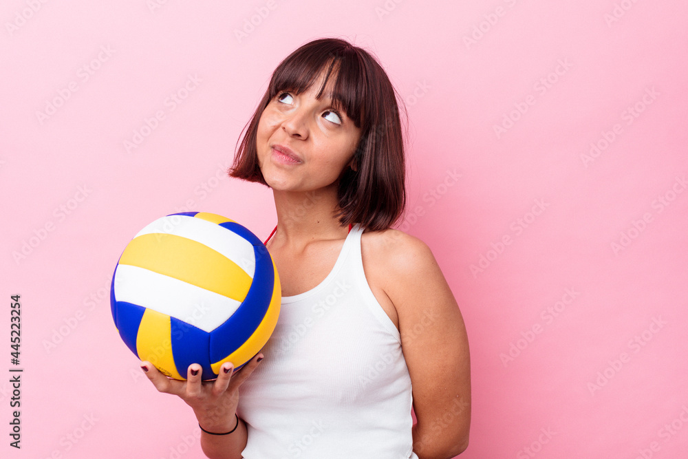 Young mixed race woman playing volleyball isolated on pink background dreaming of achieving goals and purposes