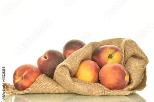 Several ripe organic peaches with a bag of jute, close-up, isolated on white.