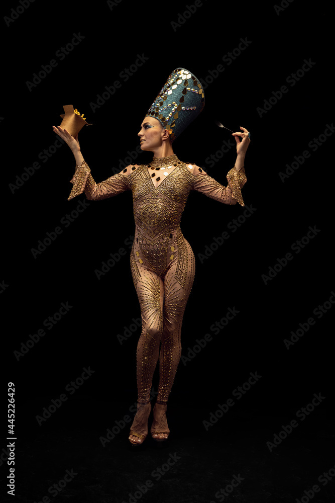 Young beautiful woman in image of Nefertiti in art performance tasting modern fast food isolated on dark background. Retro style, comparison of eras, humor concept. Young beautiful woman in image of Nefertiti in art performance tasting modern fast food isolated on dark background. Retro style, comparison of eras, humor concept.