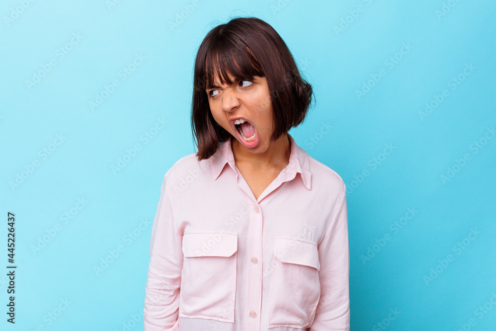 Young mixed race woman isolated on blue background shouting very angry, rage concept, frustrated. Young mixed race woman isolated on blue background shouting very angry, rage concept, frustrated.