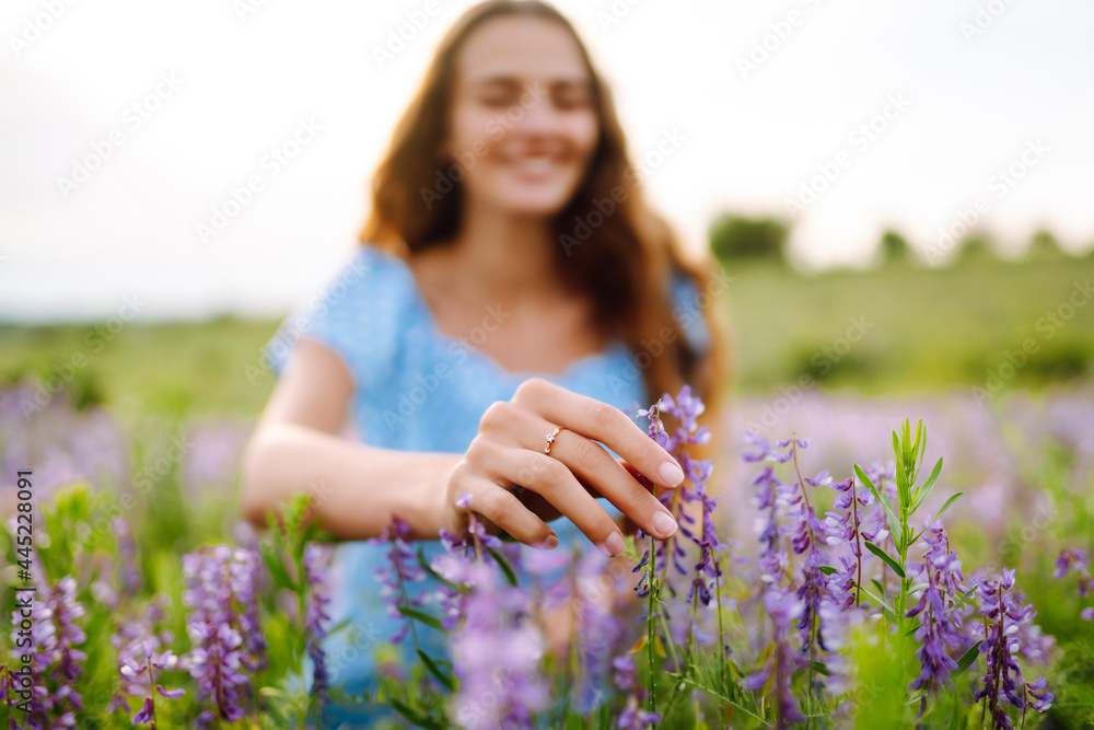 Young woman in stylish summer dress feeling free in the field with flowers in sunshine. Nature, vacation, relax and lifestyle. Summer landscape.