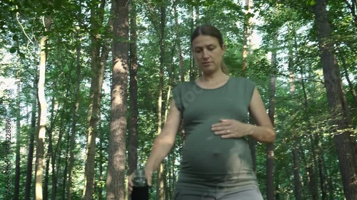 Active pregnant woman with huge belly walking on path in summer forest. Expectant mother enjoying nature outside. Pregnancy exercising healthy lifestyle concept.