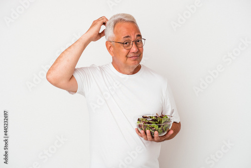 Senior american man eating salad isolated on white background being shocked, she has remembered important meeting.