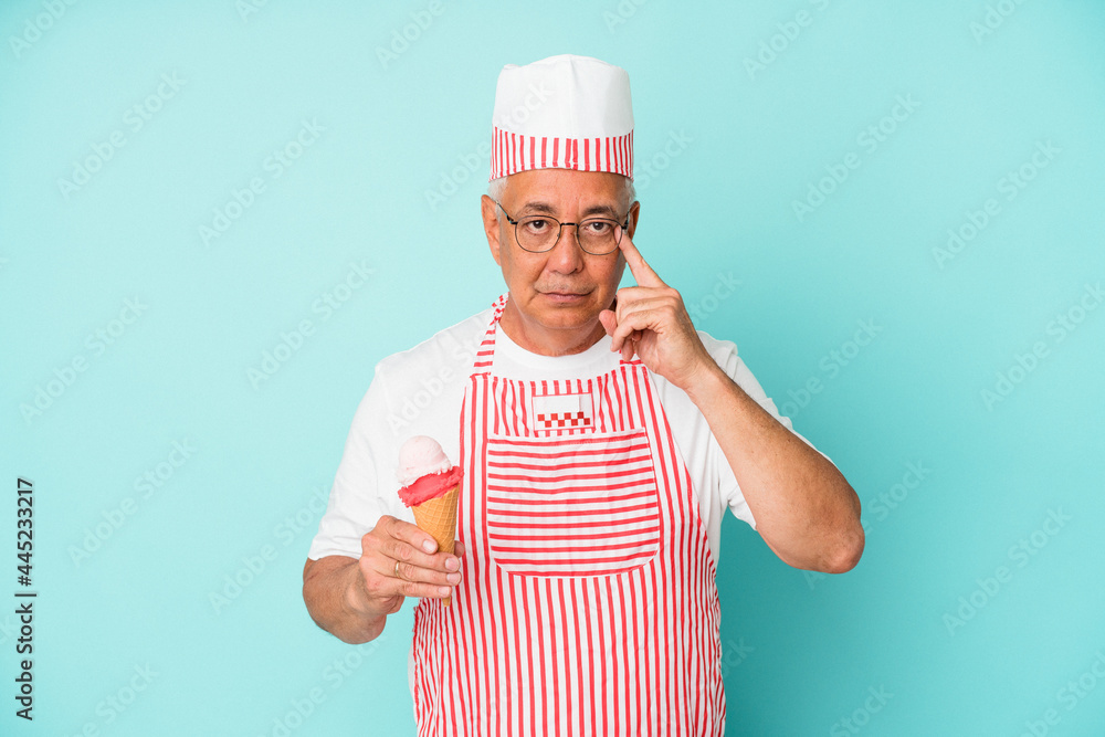 Senior american ice cream maker holding an ice cream isolated on blue background pointing temple with finger, thinking, focused on a task. Senior american ice cream maker holding an ice cream isolated on blue background pointing temple with finger, thinking, focused on a task.