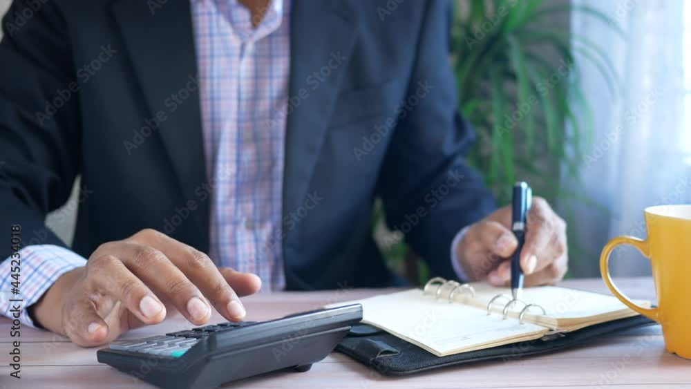 Close up of man hand using calculator and writing on notepad Close up of man hand using calculator and writing on notepad