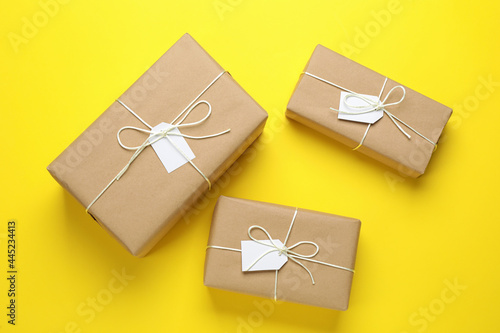 Parcels wrapped in kraft paper with tags on yellow background, flat lay