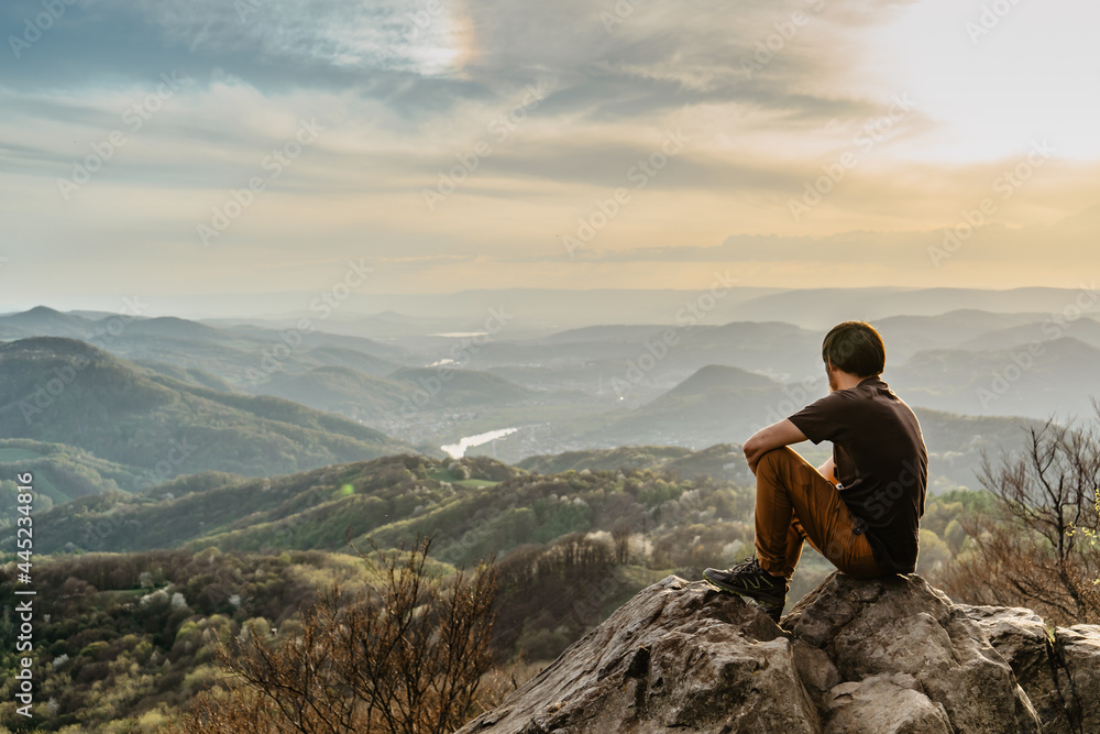 Male traveler with peaceful mind sitting on rock enjoying views of spring lush valley at sunset.Hiking day active lifestyle.Wanderlust woman relaxing outdoors.Travel freedom meditation concept