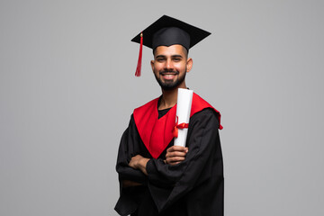 education, graduation and people concept - happy smiling indian male graduate student in mortar board and bachelor gown with diploma over grey background
