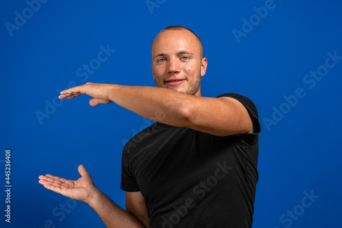 Young man with black shirt over isolated blue background holding copyspace imaginary on the palm to insert an ad. Imagination concept