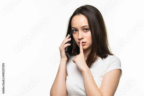 Young attractive woman holding mobile phone and showing silence gesture isolated on a gray background