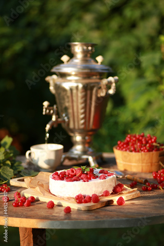 Summer atmosphere. Russian cuisine. Dacha  nature. Cottage cheese pie  cake with fresh berries  red currants and raspberries on an old wooden table. Samovar with a cup. Background image  copy space