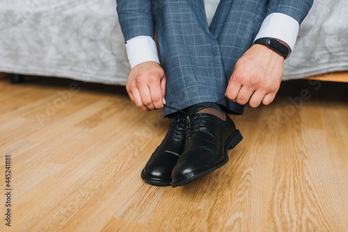 A man, a businessman, ties his shoelaces with his hands on black shiny leather shoes, getting ready for work. Photography, concept, top view.