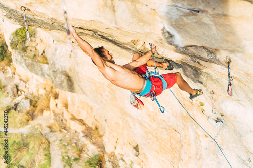 Rock climber holding himself with one arm extended upward on the rock