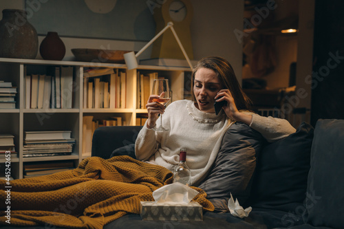 stressed woman talking on mobile phone. she is alone at home drinking alcohol