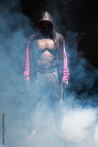 Muscular adult male in hooded jacket with bare torso with smoke around