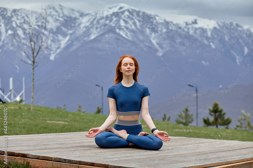 Healthy beautiful woman meditating in yoga position outdoors. Beautiful red-haired woman relaxing, meditating in nature park, sitting, namaste concept. portrait