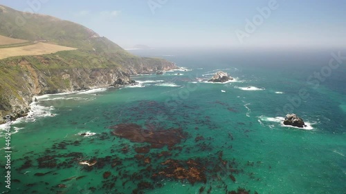 Aerial view of the California coastline near Big Sur State Park. Cliff edges can be seen as well as turquoise ocean water with algae.