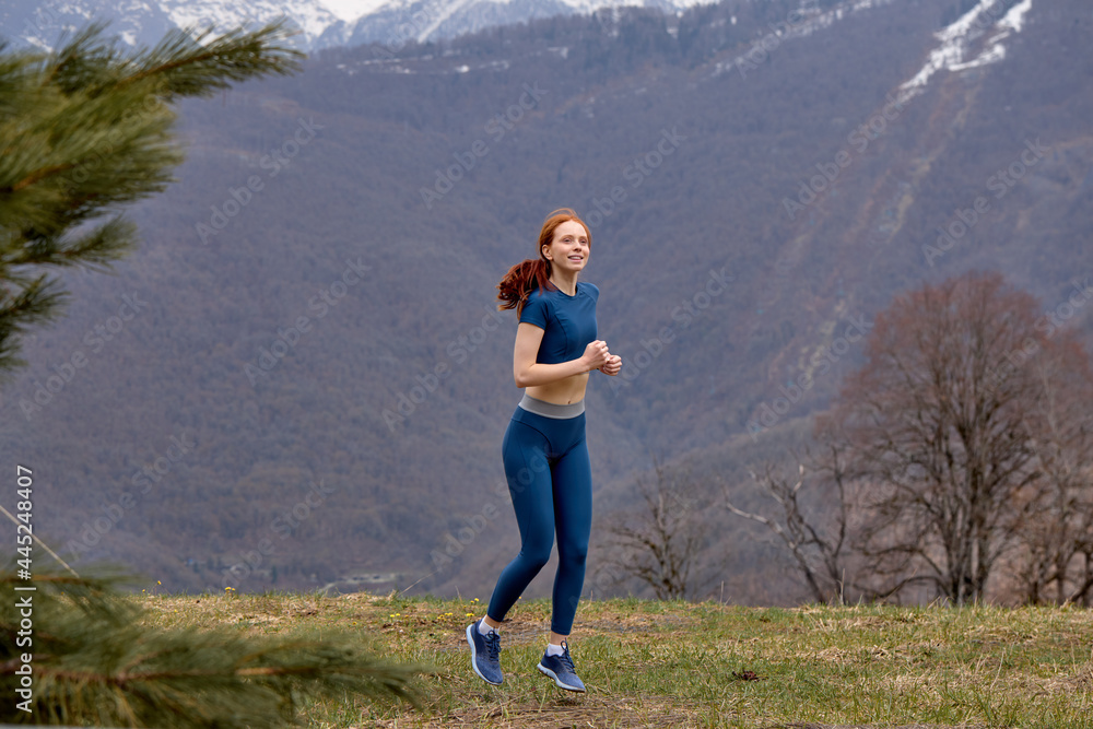 Obraz premium Jogging. Red-haired fit Female Runner Jogging during Outdoor Workout in nature in mountains. Beautiful woman in sportswear. Fitness model outdoors. Weight Loss. Healthy lifestyle. Morning