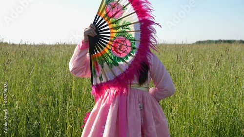Korean woman in a national costume dances a fan dance on a field with grass