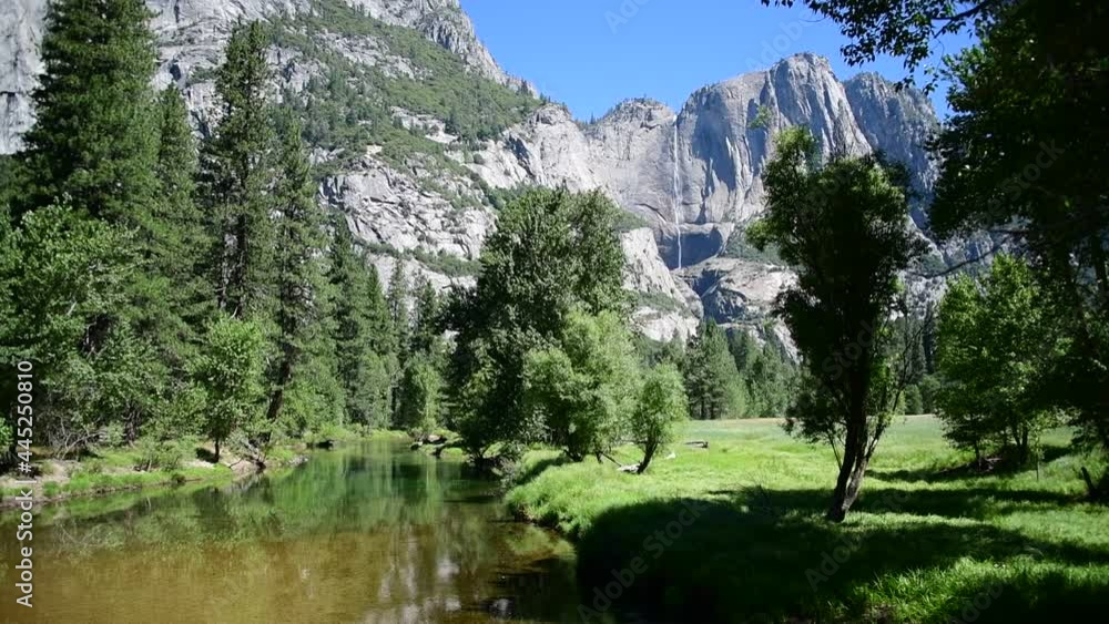 View of a waterfall in Yosemite Valley in Yosemite National Park, California. Peaks, trees, a pond, and a rock face can be seen. View of a waterfall in Yosemite Valley in Yosemite National Park, California. Peaks, trees, a pond, and a rock face can be seen.