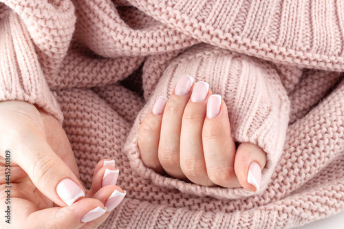 Fingernails with trendy french manicure. Beautiful female hands shooted above knitted pastel pink sweater.