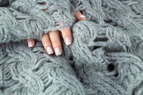 One feminine hand with beautiful stylish french manicure touching warm knitted pastelgreen blanket. Tactility concept, cozy and comfort.