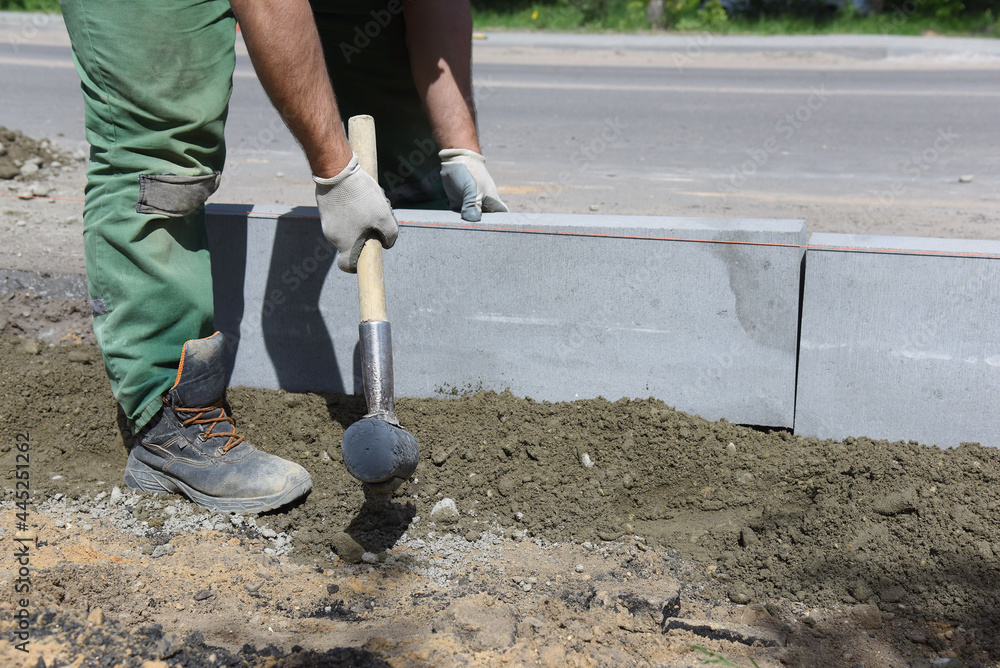 A worker knocks with a hammer on a concrete block, aligns curbs installed in cement, construction of a ring road. A worker knocks with a hammer on a concrete block, aligns curbs installed in cement, construction of a ring road.