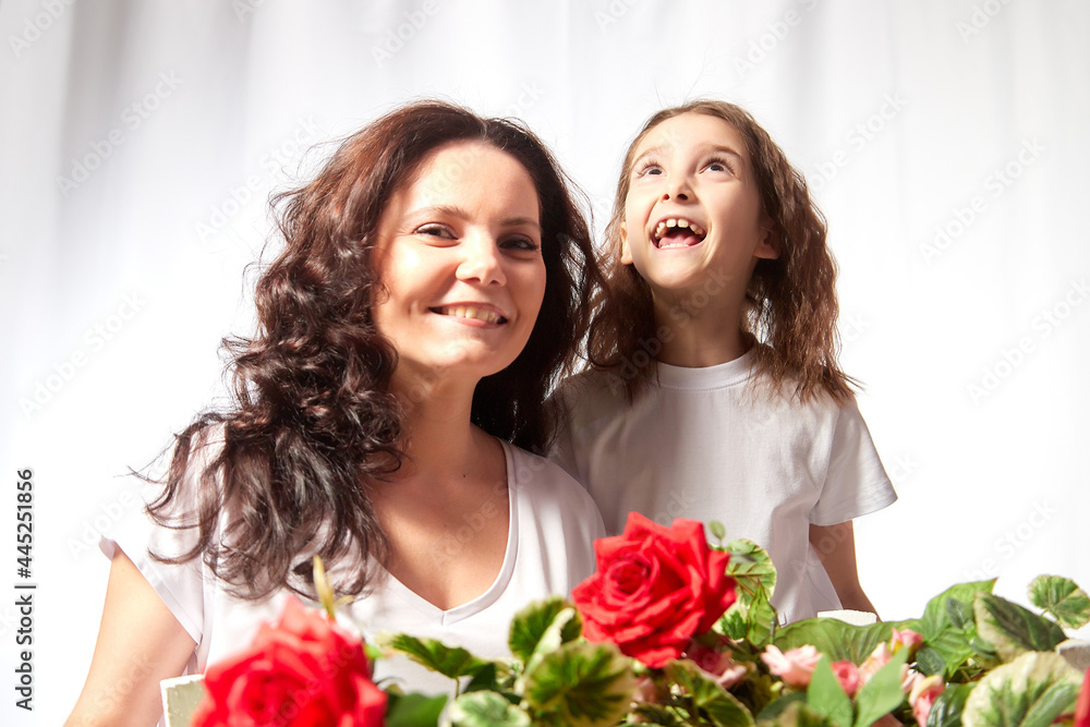 Daughter and mother with flowers in the studio on a white background. Teenager girl and woman posing indoors. Family during photo shoot in summer or spring time Daughter and mother with flowers in the studio on a white background. Teenager girl and woman posing indoors. Family during photo shoot in summer or spring time