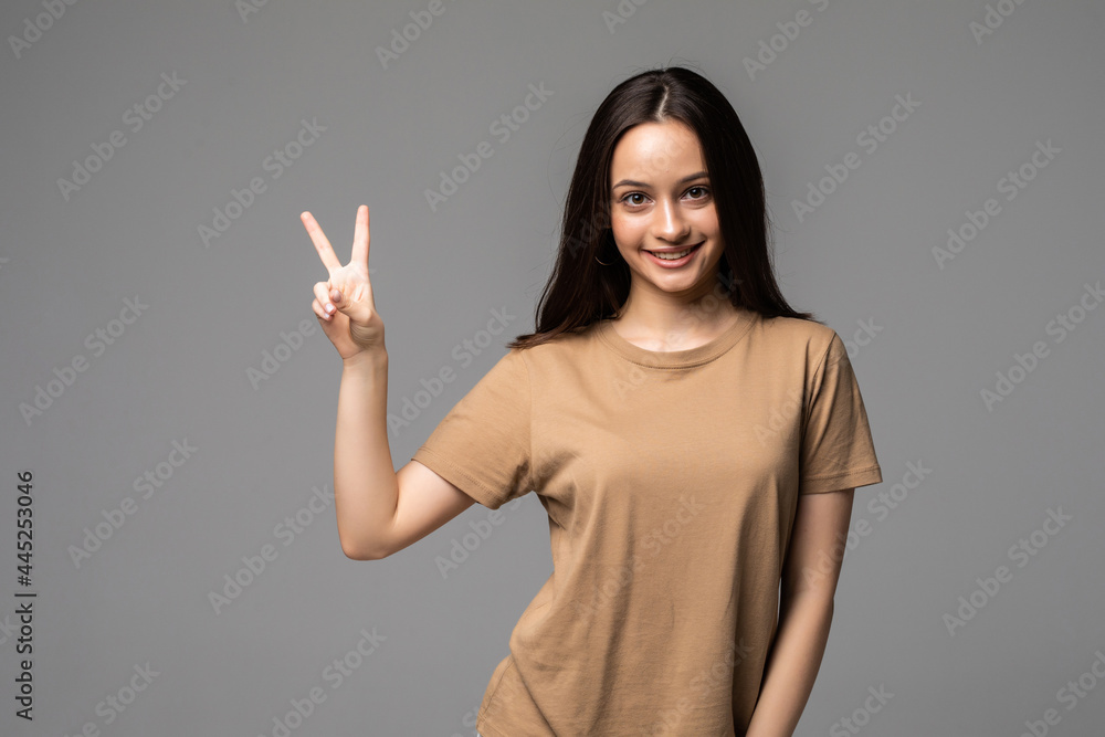 Cheerful female making a victory sign with fingers while looking at you smiling in white background Cheerful female making a victory sign with fingers while looking at you smiling in white background