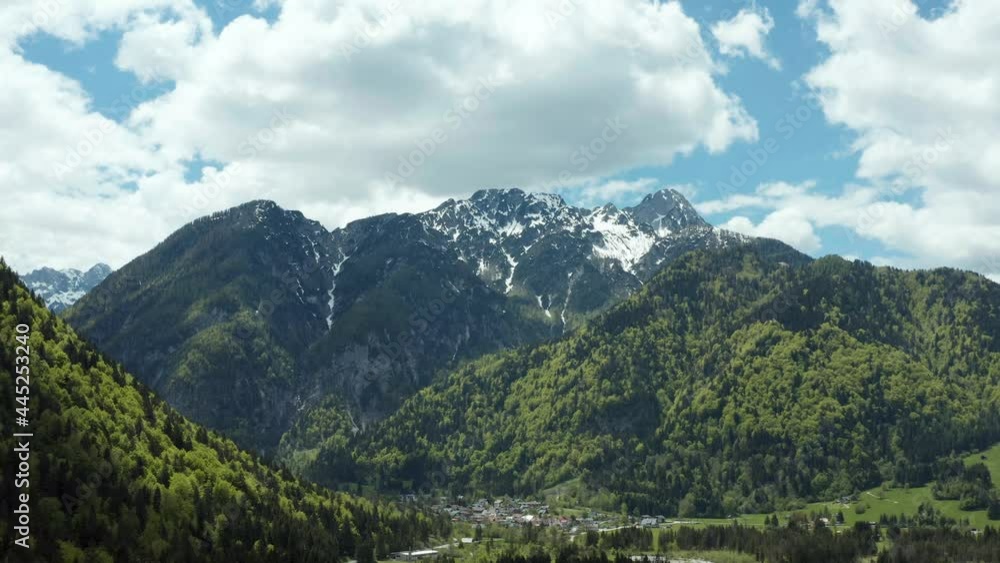 Aerials of huge peaks covered with snow, steep cliffs and green forest. White clouds on blue sky. Beautiful scenery aerial drone video 4K. Aerials of huge peaks covered with snow, steep cliffs and green forest. White clouds on blue sky. Beautiful scenery aerial drone video 4K.