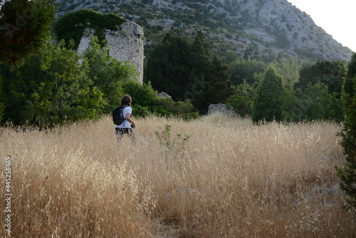 A young man walks on a field on a background of mountains and the ruins of an old castle