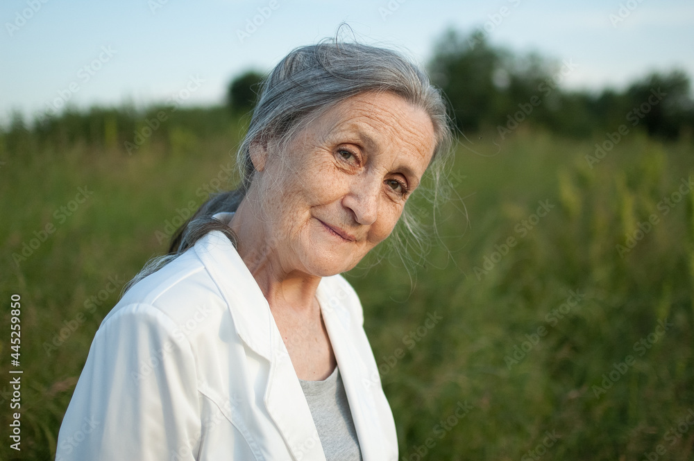 Portrait of senior woman with grey hair and face with wrinkles wearing white jacket and relaxing at park during sunny weather, mothers day Portrait of senior woman with grey hair and face with wrinkles wearing white jacket and relaxing at park during sunny weather, mothers day