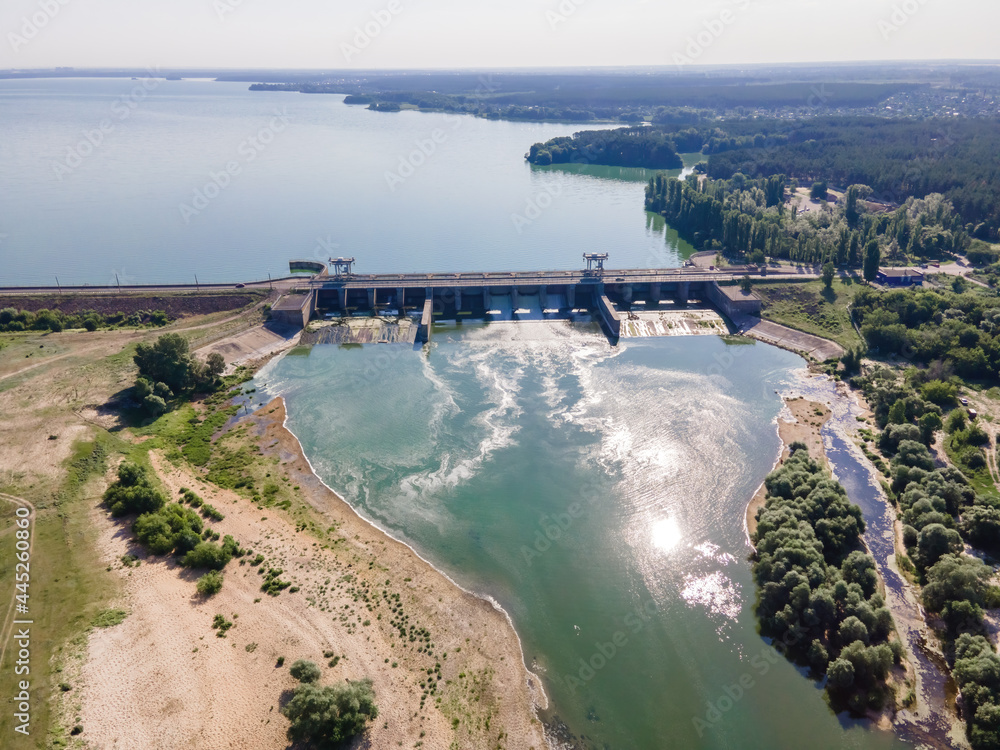 Dam with flowing water at hydroelectric power station at reservoir lake of river. Aerial view