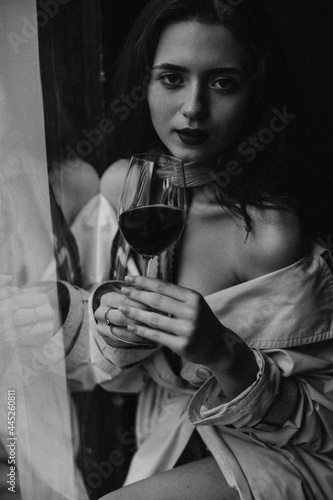 Beautiful woman looking into camera and holding wine glass. Black and white portrait of charming lady posing in bar
