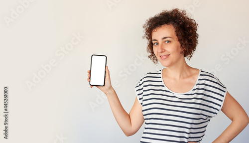 A woman poses next to her mobile phone, looking at the camera
